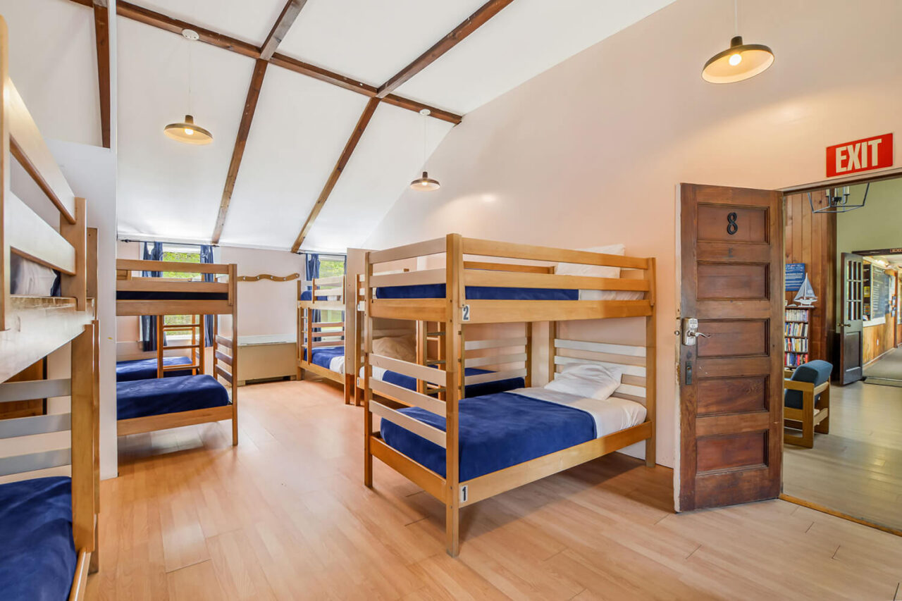 a large, airy women's dorm room at HI Martha's Vineyard hostel with eight sets of twin-sized bunk beds, high ceilings, wood floors, and windows letting in natural light.