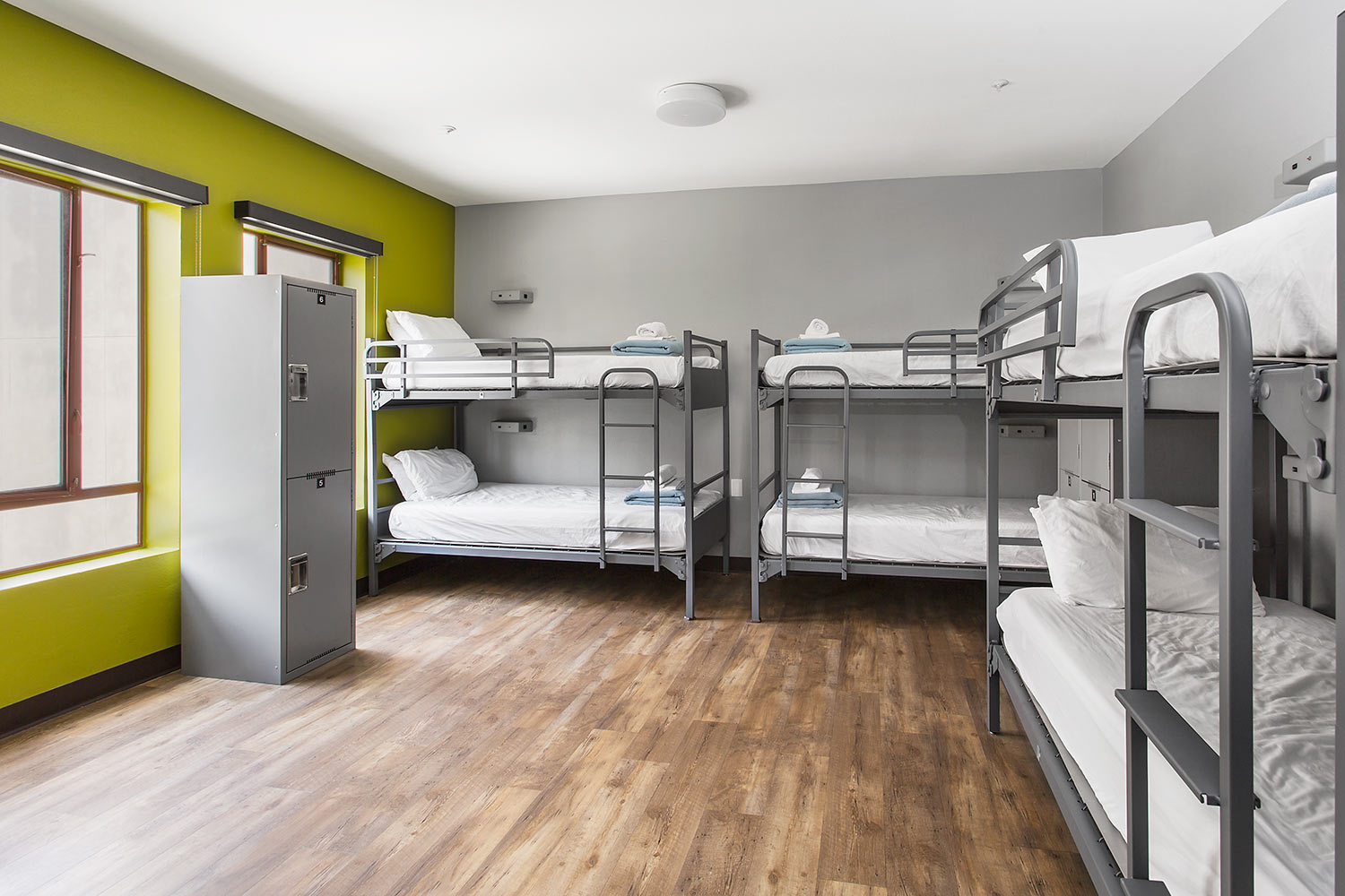 a newly remodeled dorm room at HI Los Angeles Santa Monica hostel, with three sets of freshly made twin-sized bunk beds and individual secure lockers for guest belongings