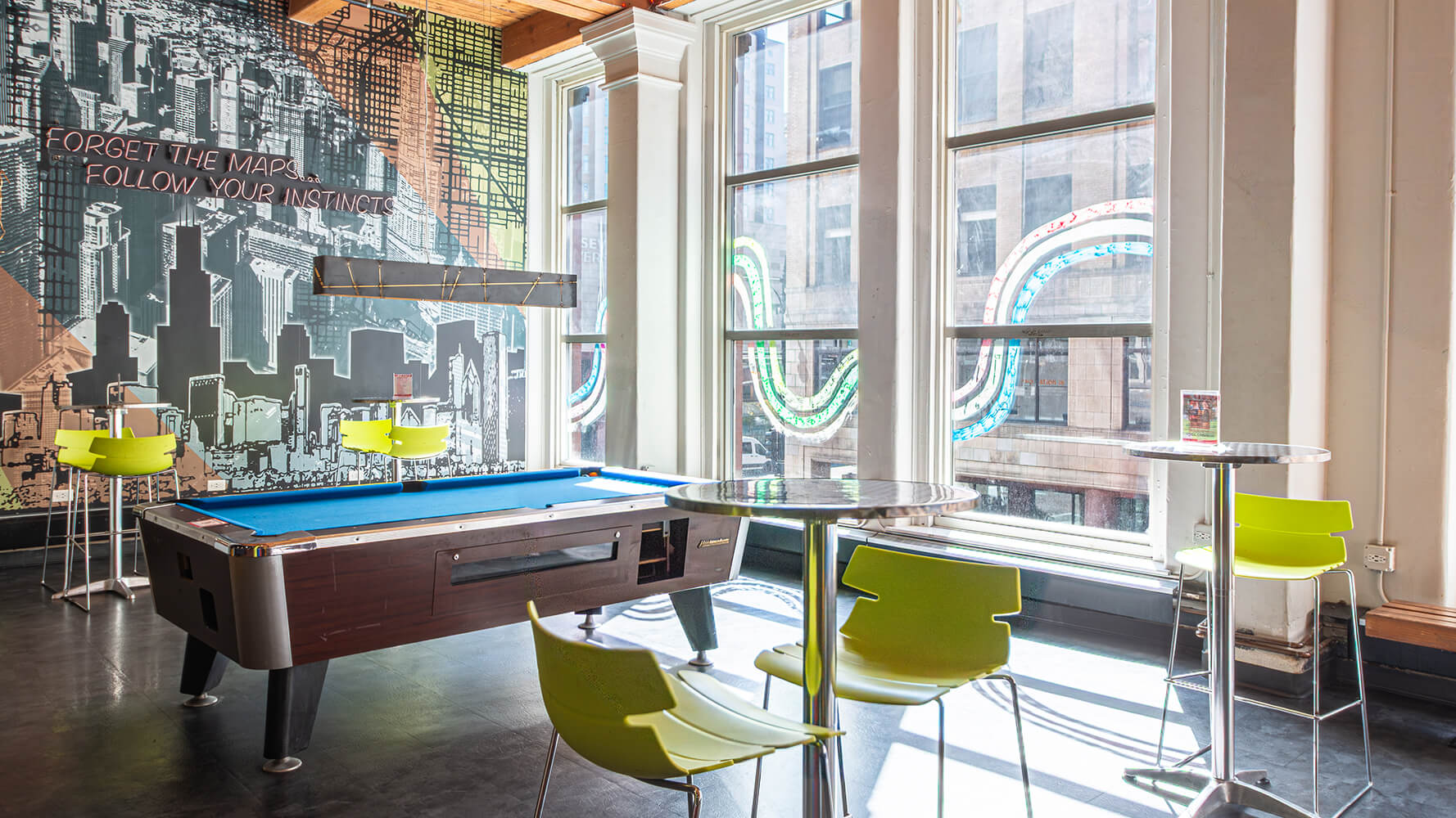The spacious guest lounge at HI Chicago hostel features a pool table, floor-to-ceiling windows, and high-top tables and chairs