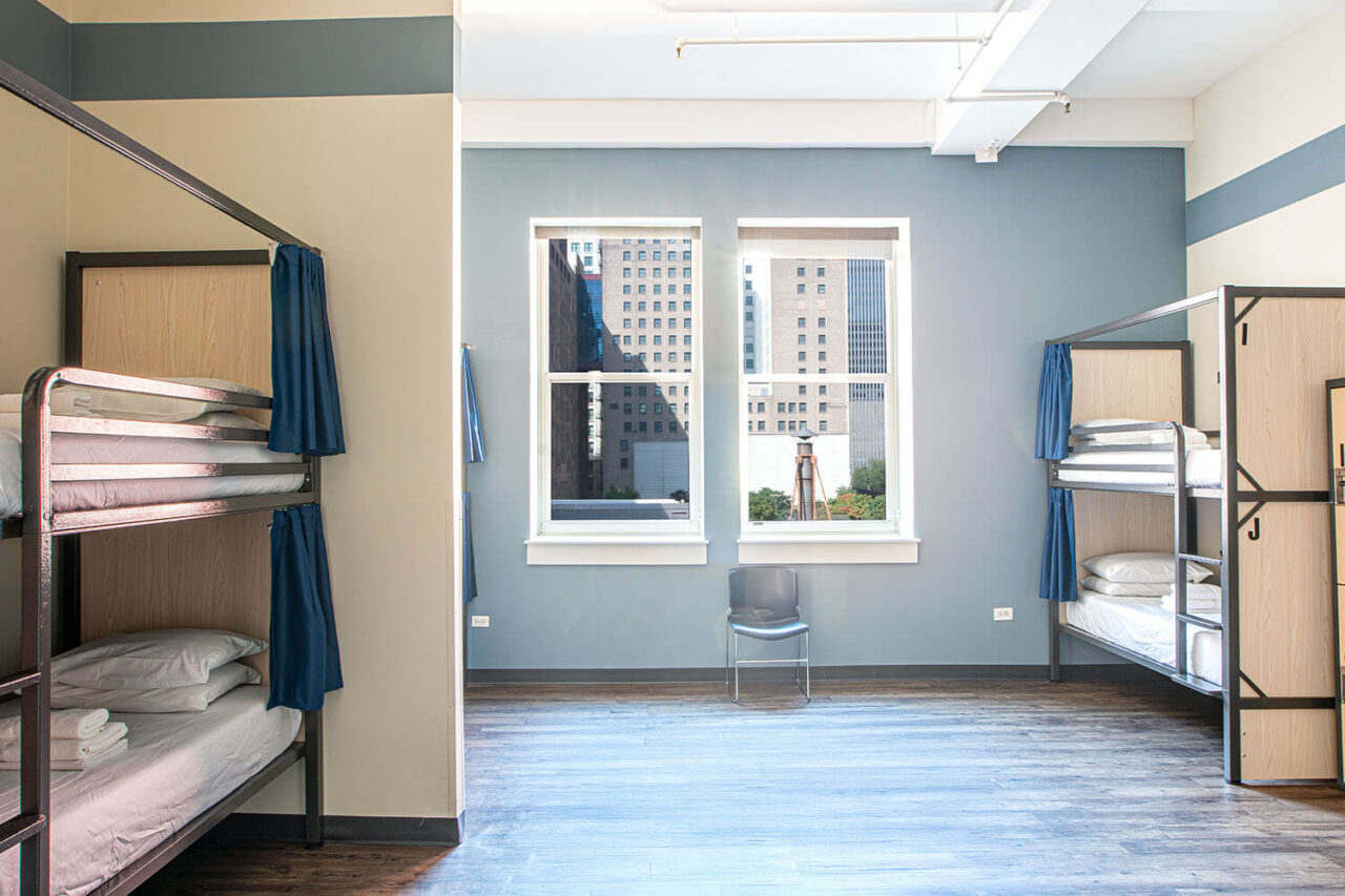 A spacious 10-bed dorm room at HI Chicago hostel with five sets of bunk beds and two large windows letting in natural light.