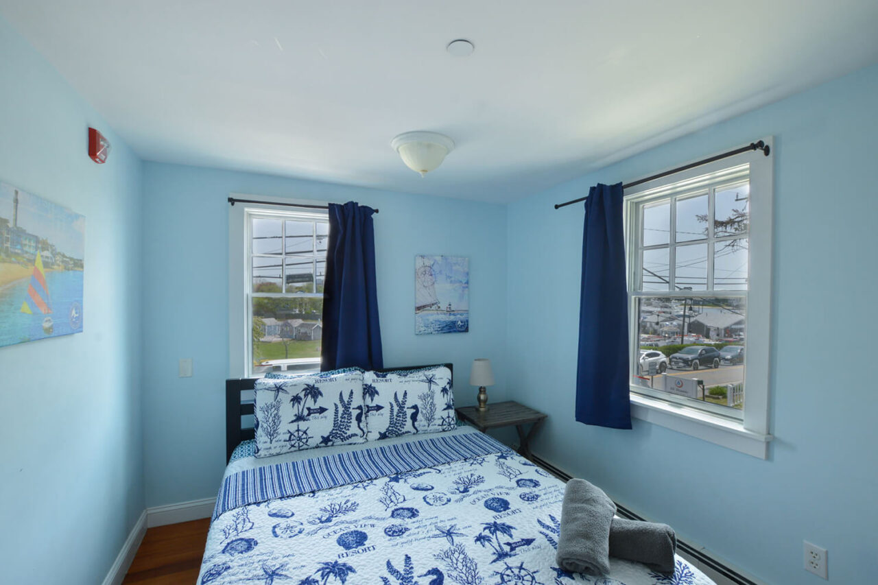 a freshly made queen-sized bed in a private room at HI Hyannis hostel on cape cod. There are two windows in the room overlooking the Hyannis Harbor.