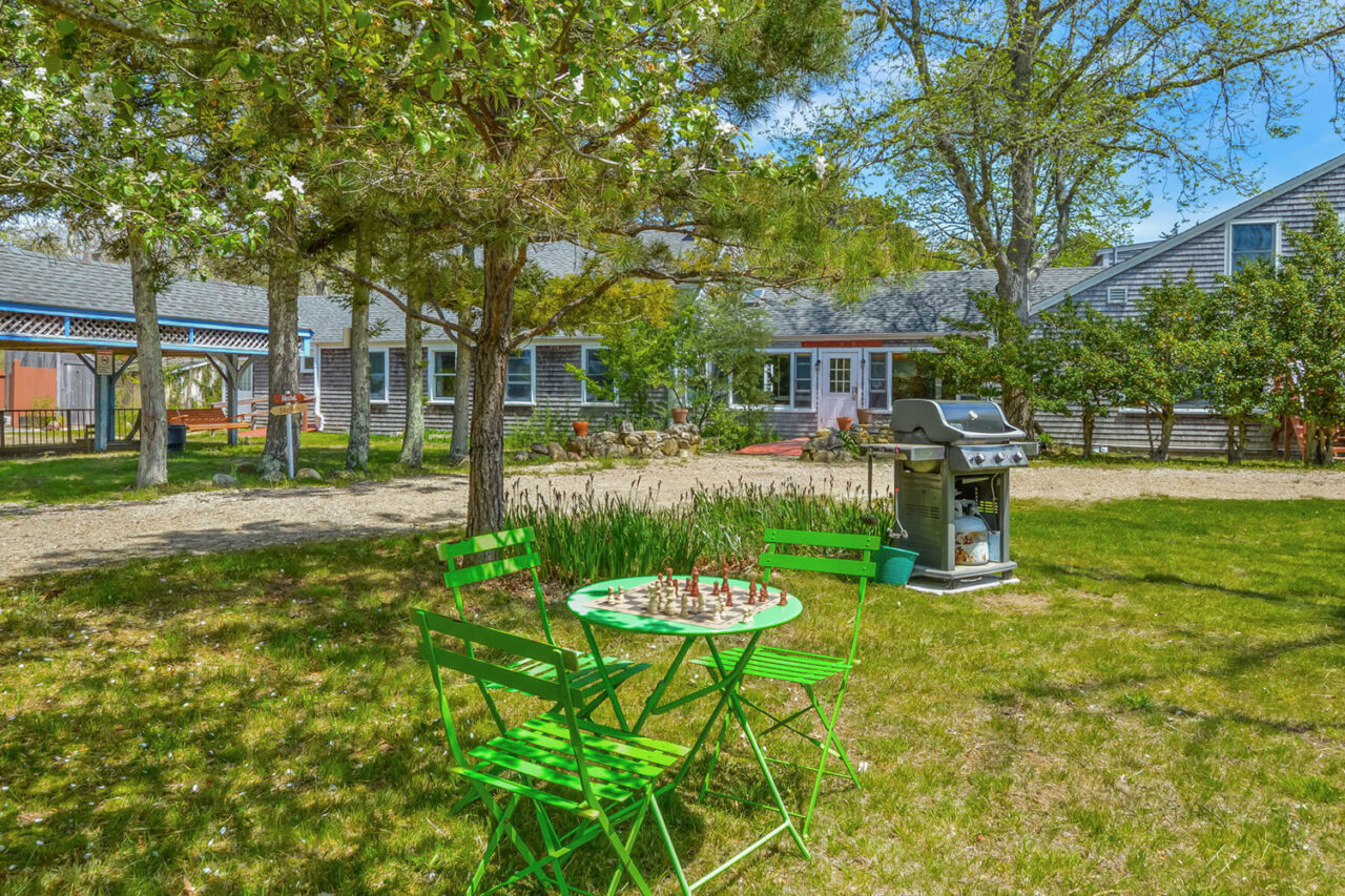 The front lawn at HI Martha's Vineyard hostel featuring a cafe table and chairs in the shade and a large gas grill for guest use