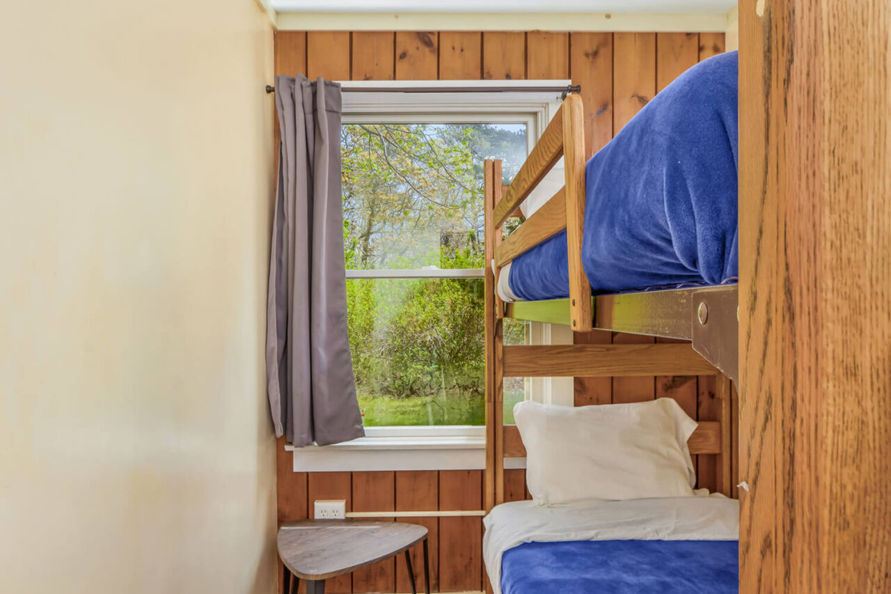 A small private room at HI Martha's Vineyard hostel with one set of twin-sized bunk beds and a window overlooking the front yard.