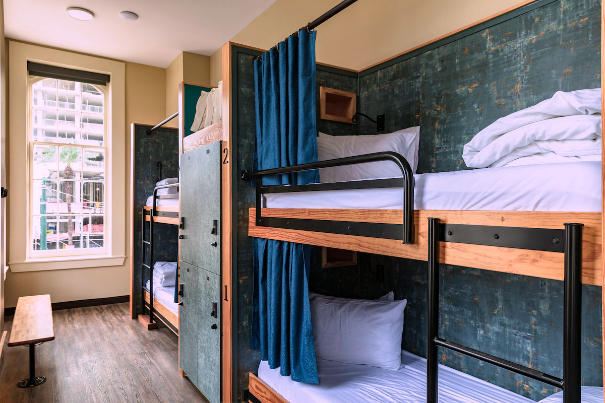 A dorm room at HI New Orleans hostel with two sets of twin-sized bunk beds, individual secure lockers for guest belongings, hardwood floors, and a large window