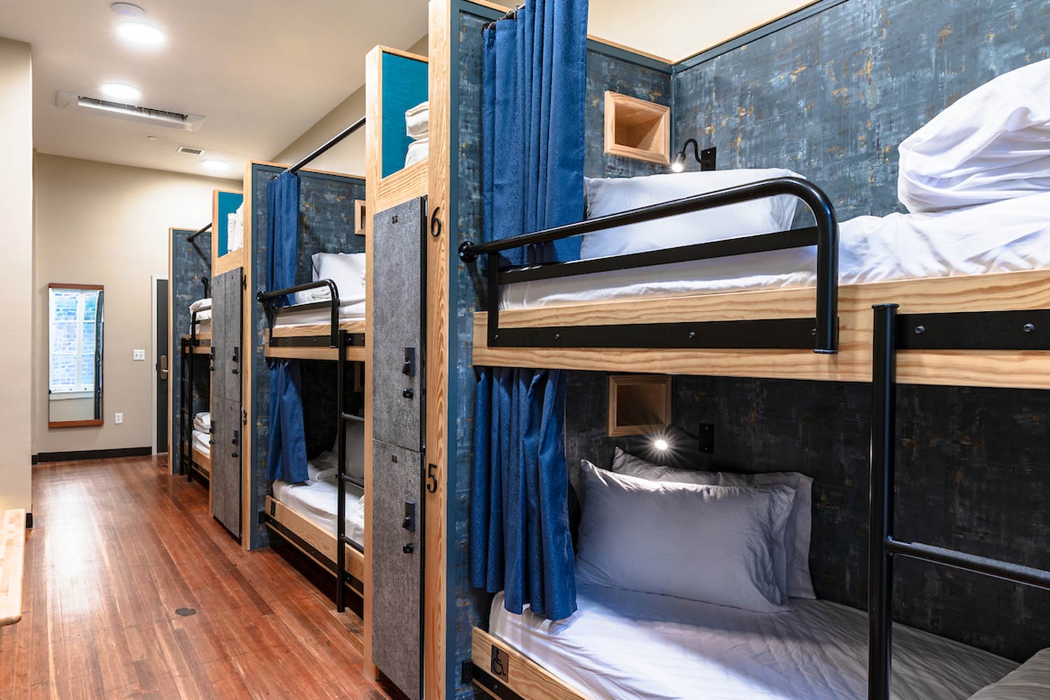 A dorm room at HI New Orleans hostel with three sets of twin-sized bunk beds, individual secure lockers for guest belongings, hardwood floors, and a large window