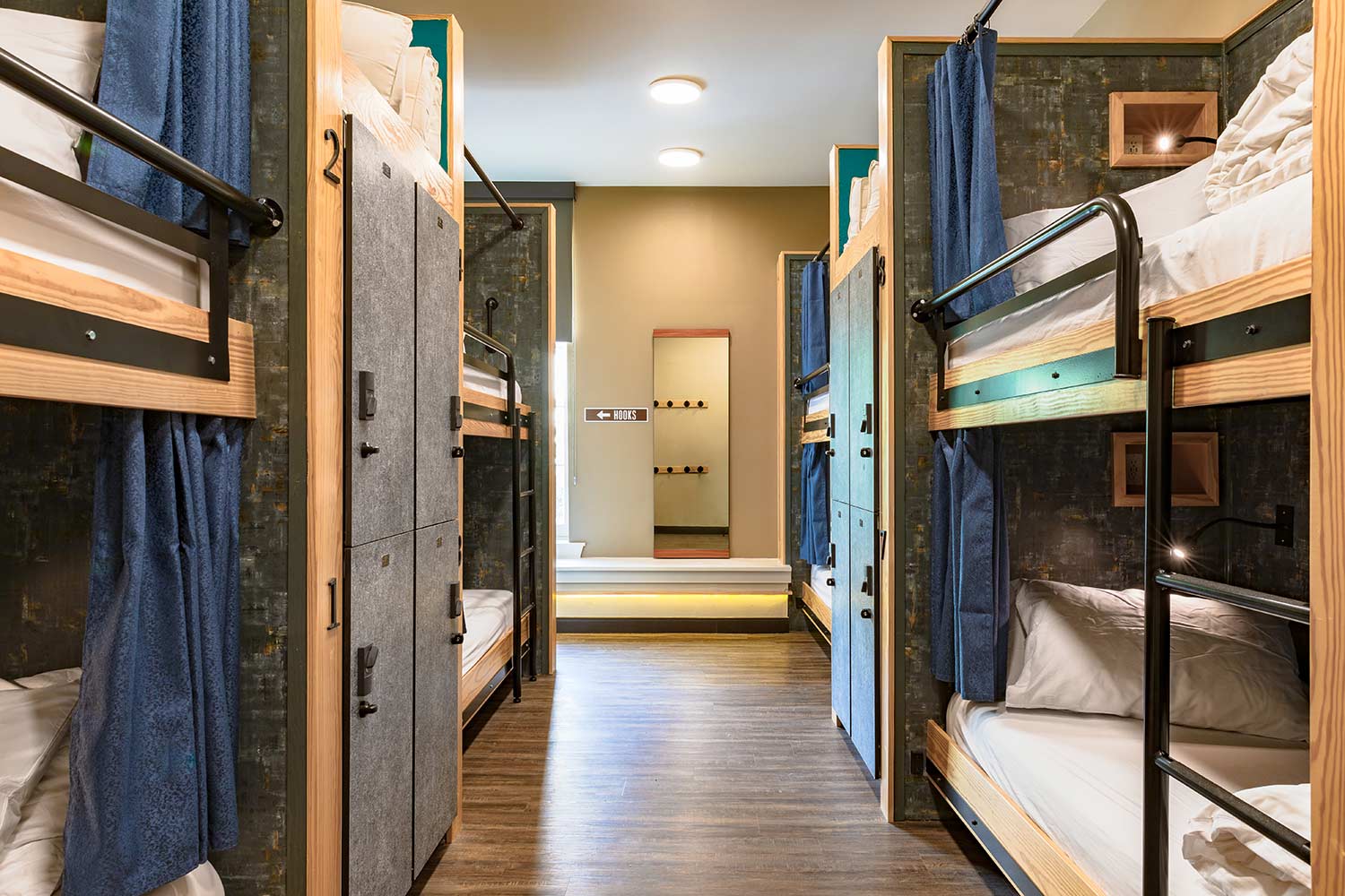 A dorm room at HI New Orleans hostel with four sets of twin-sized bunk beds, individual secure lockers for guest belongings, hardwood floors, and a large window