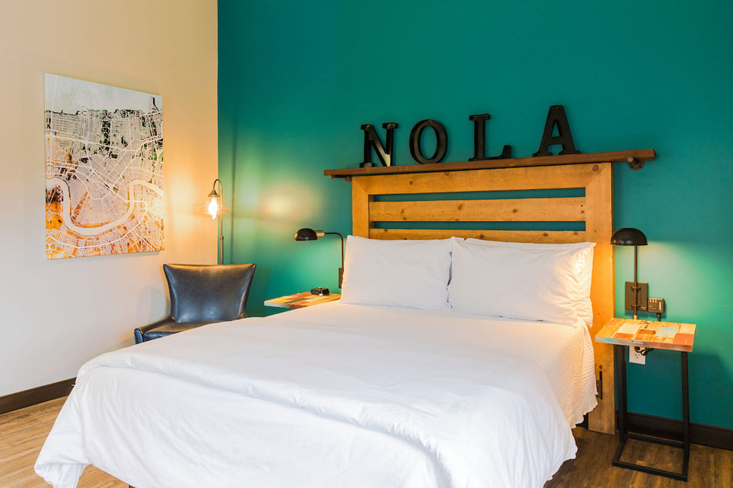 A queen-sized bed with crisp white linens and a wooden headboard against a turquoise colored wall at HI New Orleans hostel