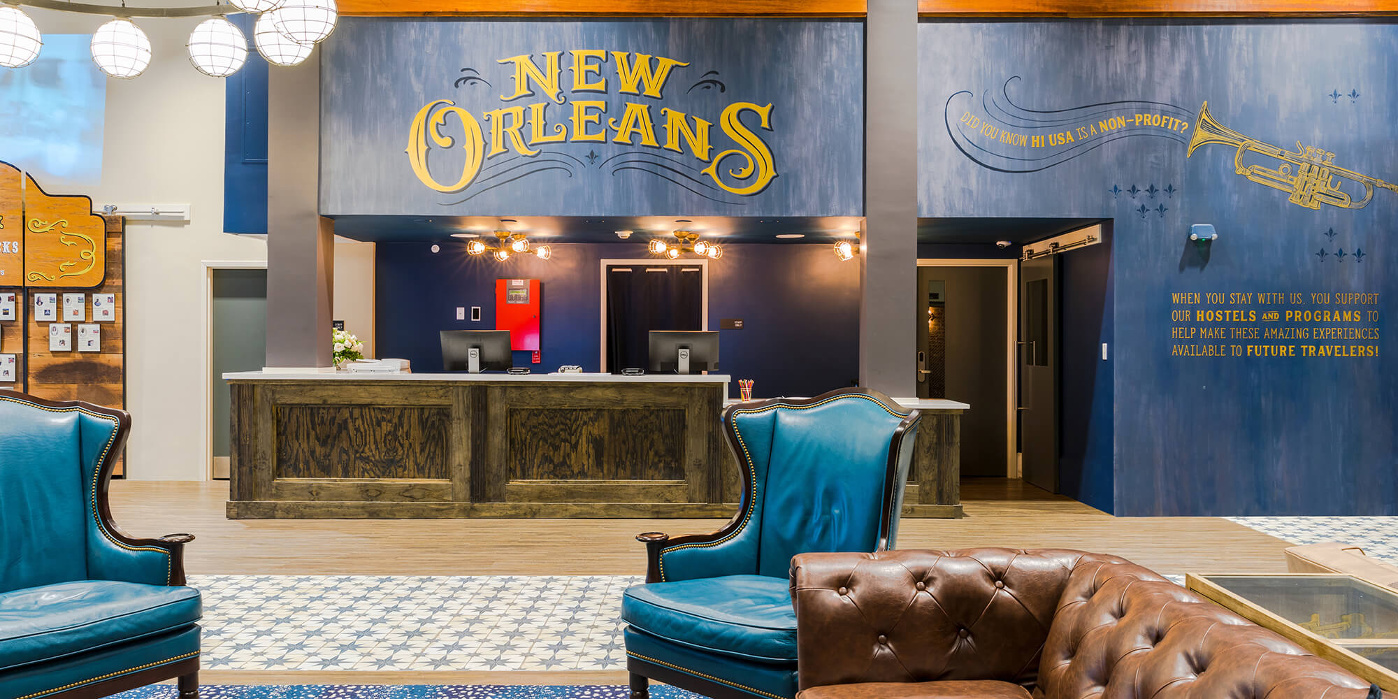 The lobby of HI New Orleans hostel and front desk, with comfortable chairs and sofas in the foreground.