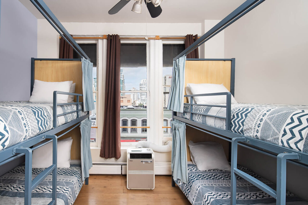 a 4-bed dorm room at HI San Diego Downtown hostel with privacy screens and curtains on each freshly made bunk and a window looking out over the Gaslamp Quarter