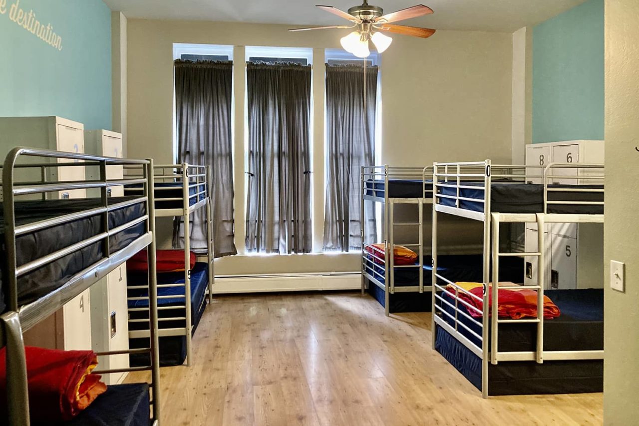a large dorm room at HI San Diego Downtown hostel with blue walls, hardwood flooring, three large windows, and four sets of twin-sized bunk beds.