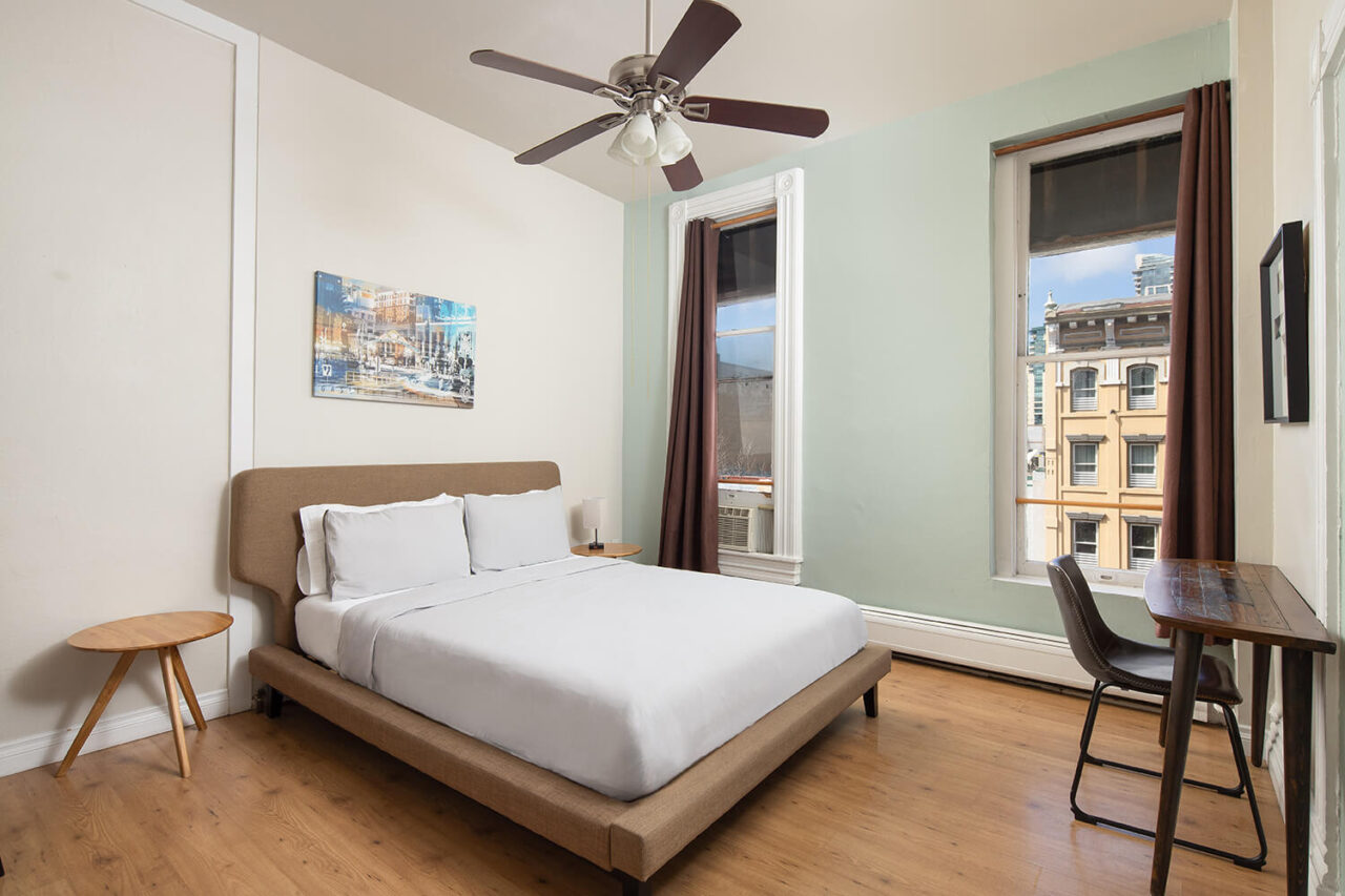 a private room at HI San Diego Downtown hostel with a freshly made full-sized bed and two windows looking out over the gaslamp quarter