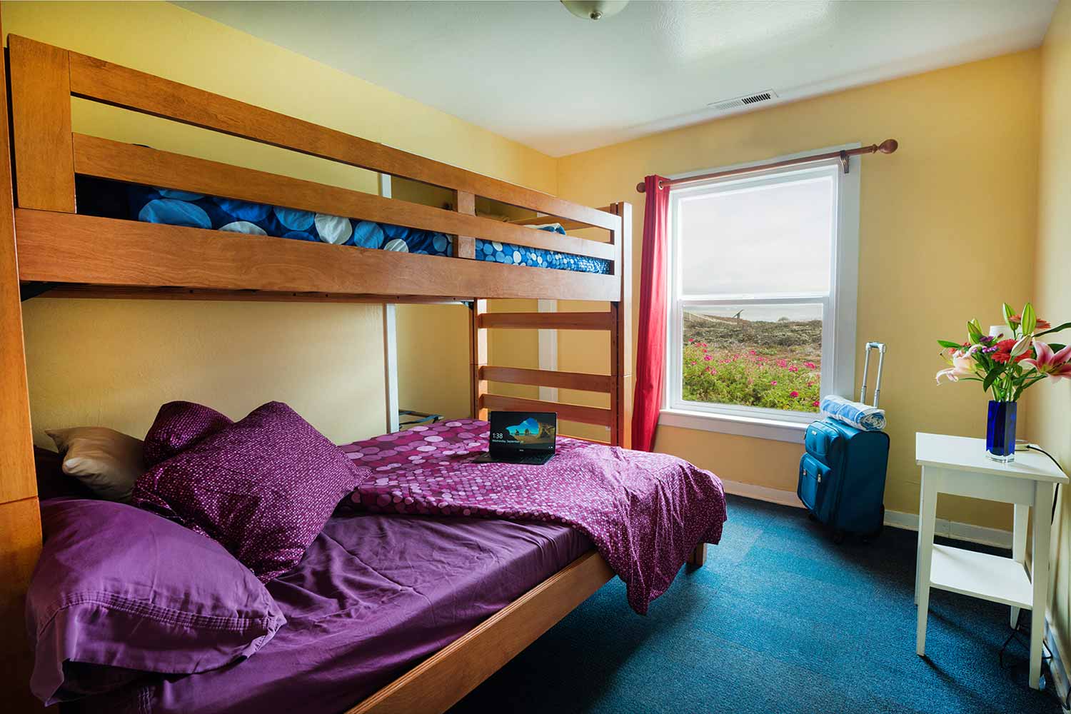 a private room at HI Pigeon Point Lighthouse hostel with one full-sized bed with one twin-sized bed bunked over it, and a window looking out over the coast.