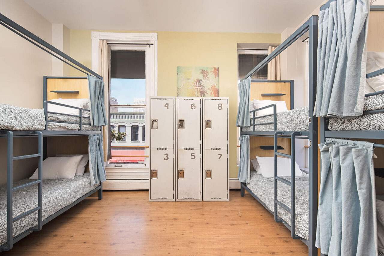 a well lit dorm room at HI San Diego Downtown hostel with three sets of bunk beds, six secure lockers, and a window overlooking the gaslamp quarter