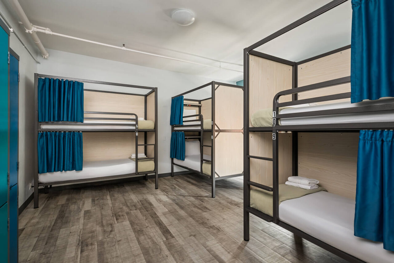 A modern shared dormitory room at HI New York City hostel. The 10-bed room features bunks with fresh white linens, privacy screens and blue curtains on each bunk.