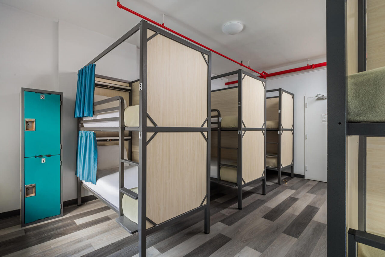 A clean and modern shared dorm room at HI New York City hostel. The room's 12 bunks each have their own privacy screens and curtains, and there are blue individual lockers for guest belongings.