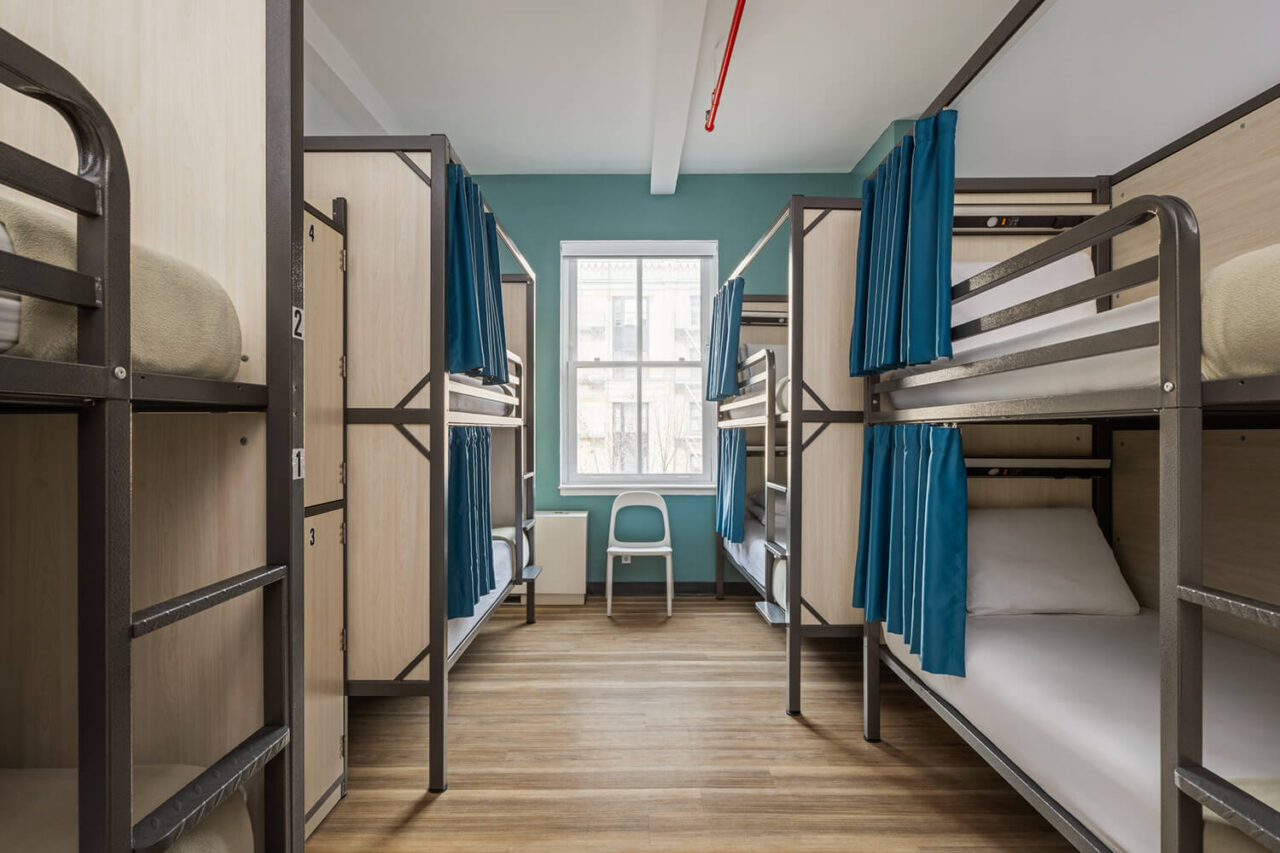 A modern shared dormitory room at HI New York City hostel. Each of the 8 bunk beds has a privacy screen and individual blue privacy curtains.