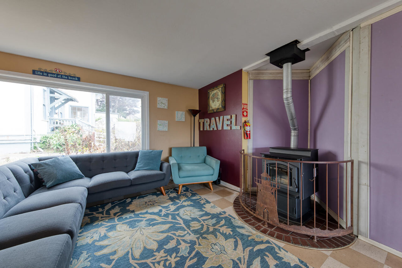 a cozy lounge with sectional sofa, armchair, and pellet fireplace in the Sea Lodge building at HI Point Montara lighthouse hostel.