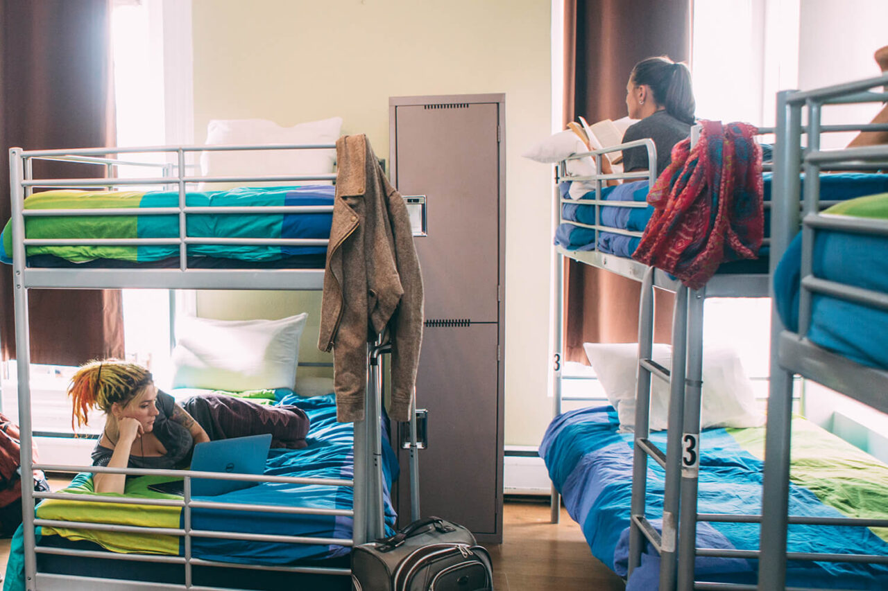three sets of freshly made bunk beds in a six-bed dorm room at HI San Diego Downtown. There are two women reading lying on different bunks.