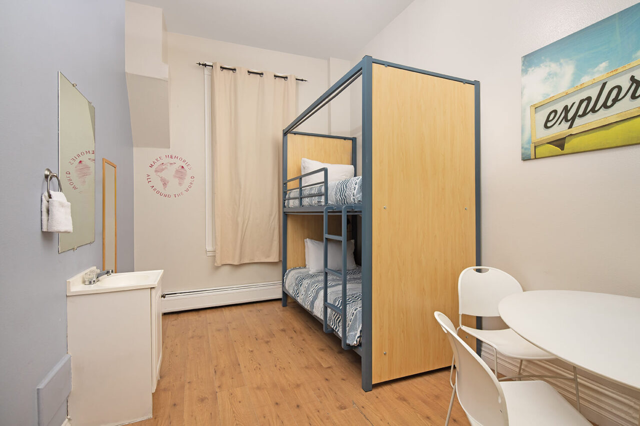 a small private room at HI San Diego Downtown hostel with one set of new, freshly made bunk beds and wood floors. At one end of the room there is a small table with two chairs, and a sink.