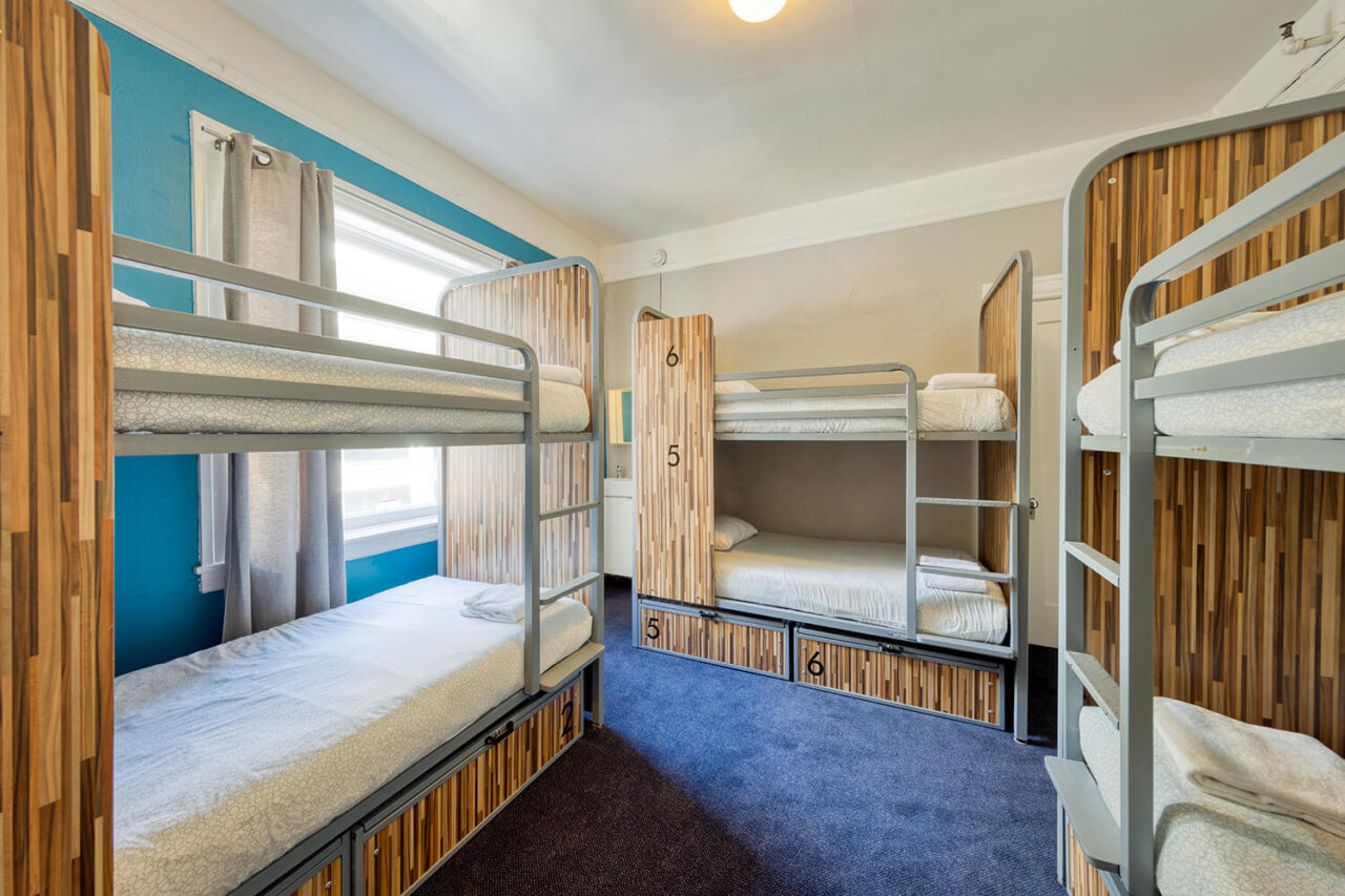 three sets of modern bunk beds with privacy screens and built-in secure luggage storage in a dorm room with royal blue carpet at HI San Francisco Downtown hostel