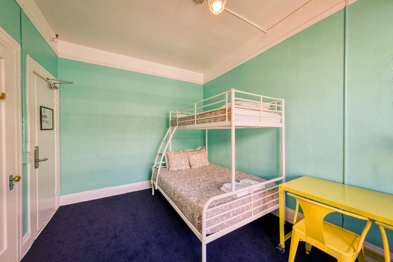 one full-sized bed with one twin-sized bed bunked over it, and a yellow desk with chairs in an economy private room at HI San Francisco Downtown hostel