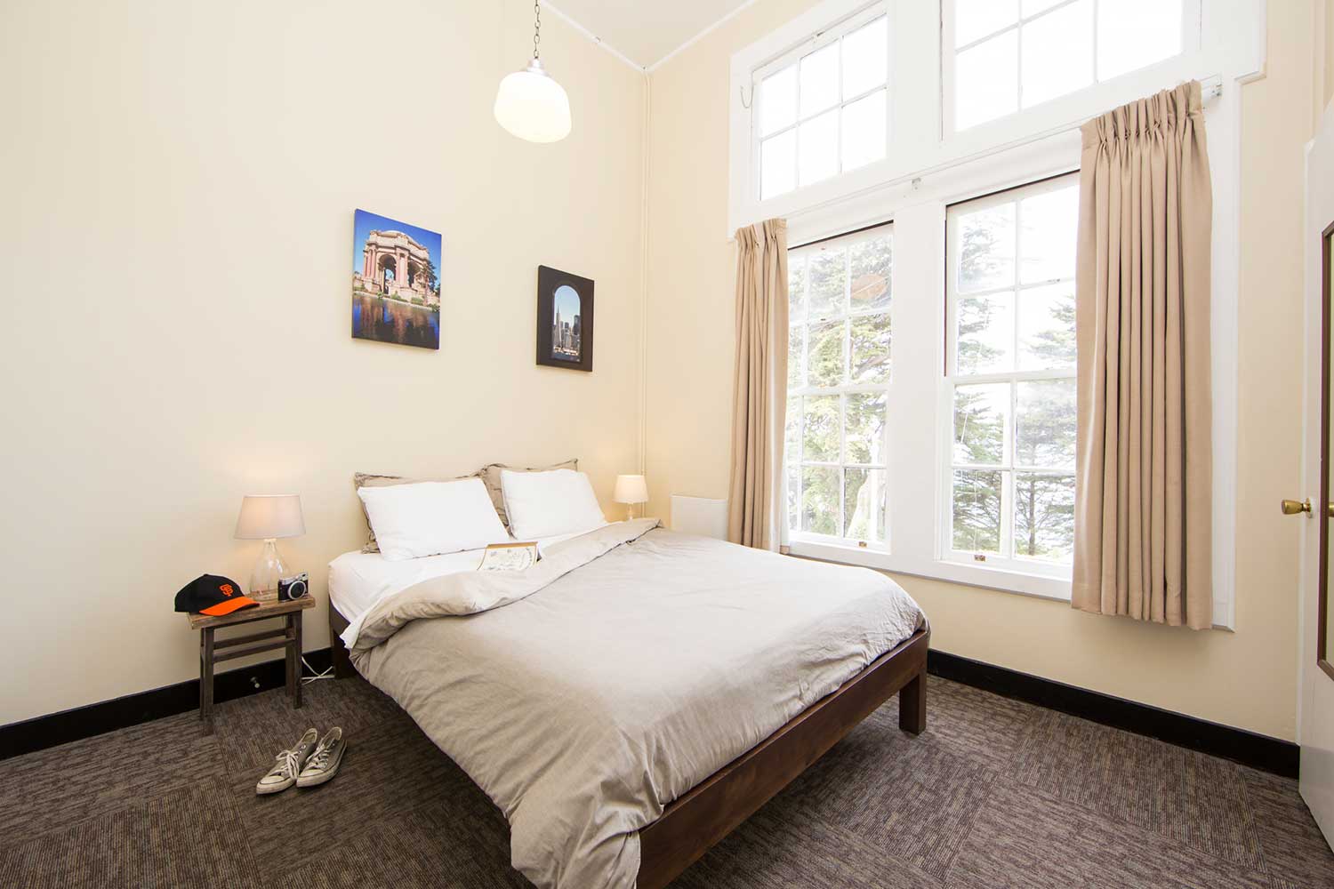 A private room at HI San Francisco Fisherman's Wharf hostel with a large freshly made bed and a window with the curtains open looking out over Monterey Cypress trees