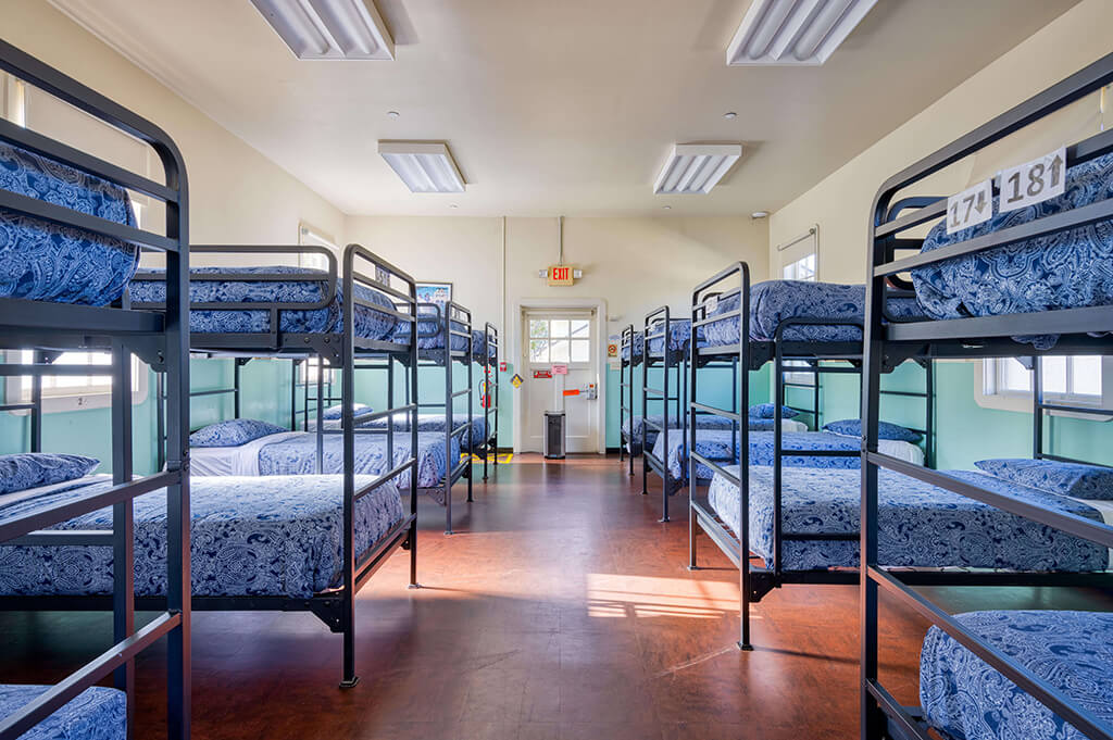 a large dorm room at HI San Francisco Fisherman's Wharf hostel with 10 sets of freshly made bunk beds with blue bedspreads
