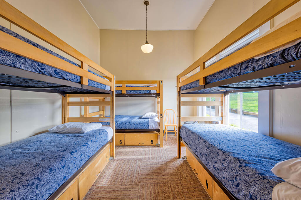 A dorm room at HI San Francisco Fisherman's Wharf hostel with three sets of freshly made bunk beds with blue bedspreads