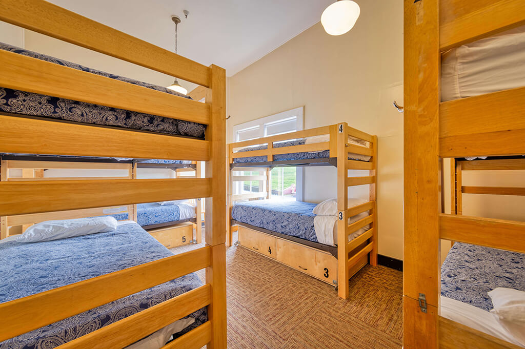 A dorm room at HI San Francisco Fisherman's Wharf hostel with four sets of freshly made bunk beds with blue bedspreads