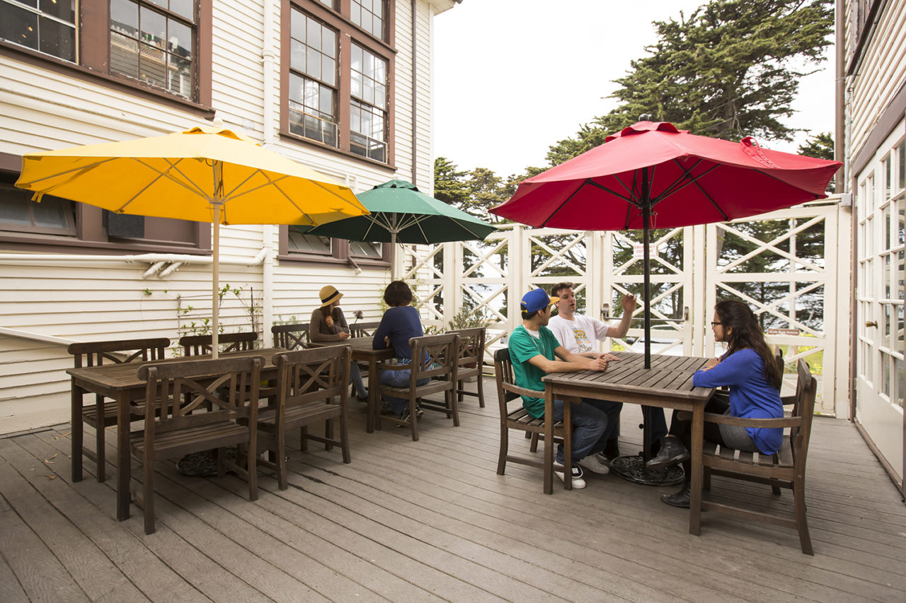 Guests relax at picnic tables under umbrellas on the private back porch at HI San Francisco Fisherman's Wharf hostel