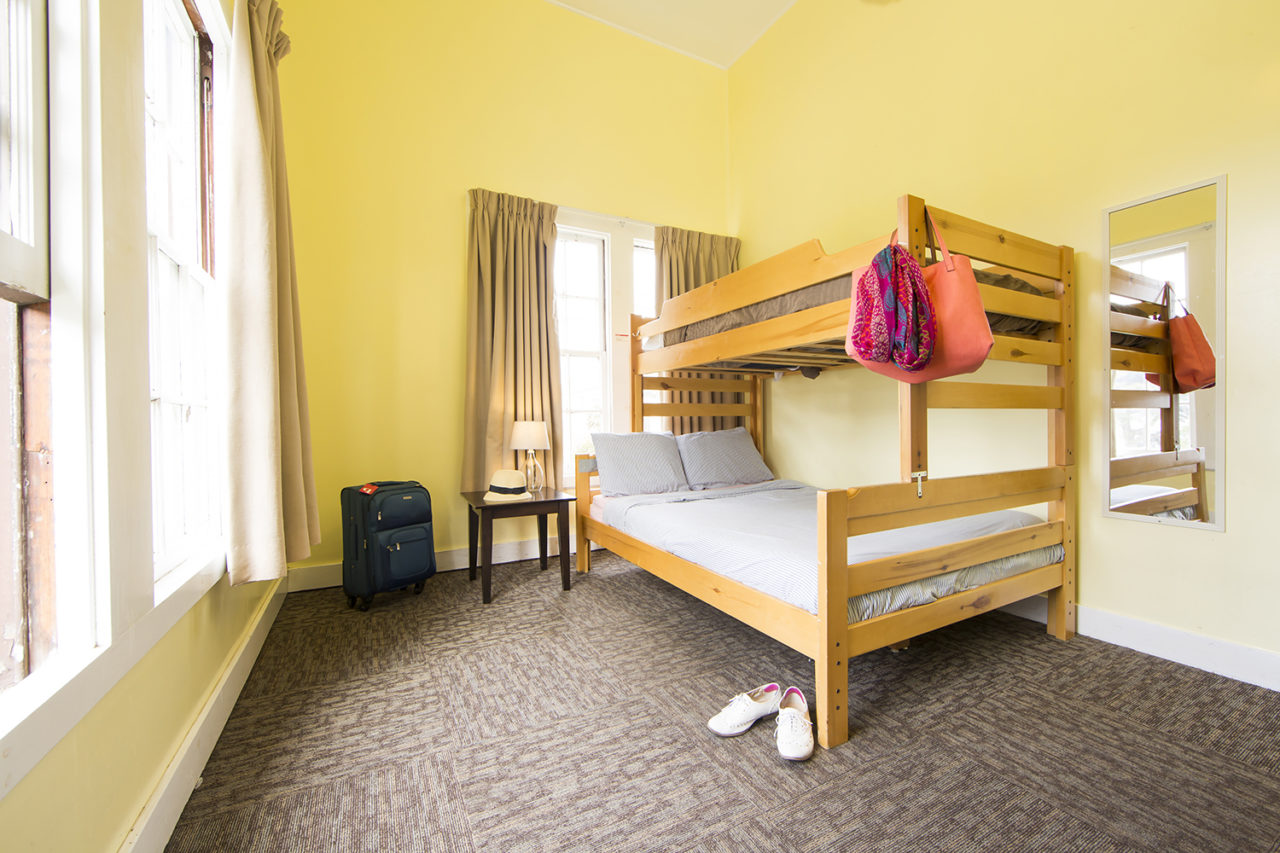 a bright private room at HI San Francisco Fisherman's Wharf hostel with a large wood-framed bed and yellow walls. There is one freshly made up full-sized bed with one twin-sized bed bunked on top of it.