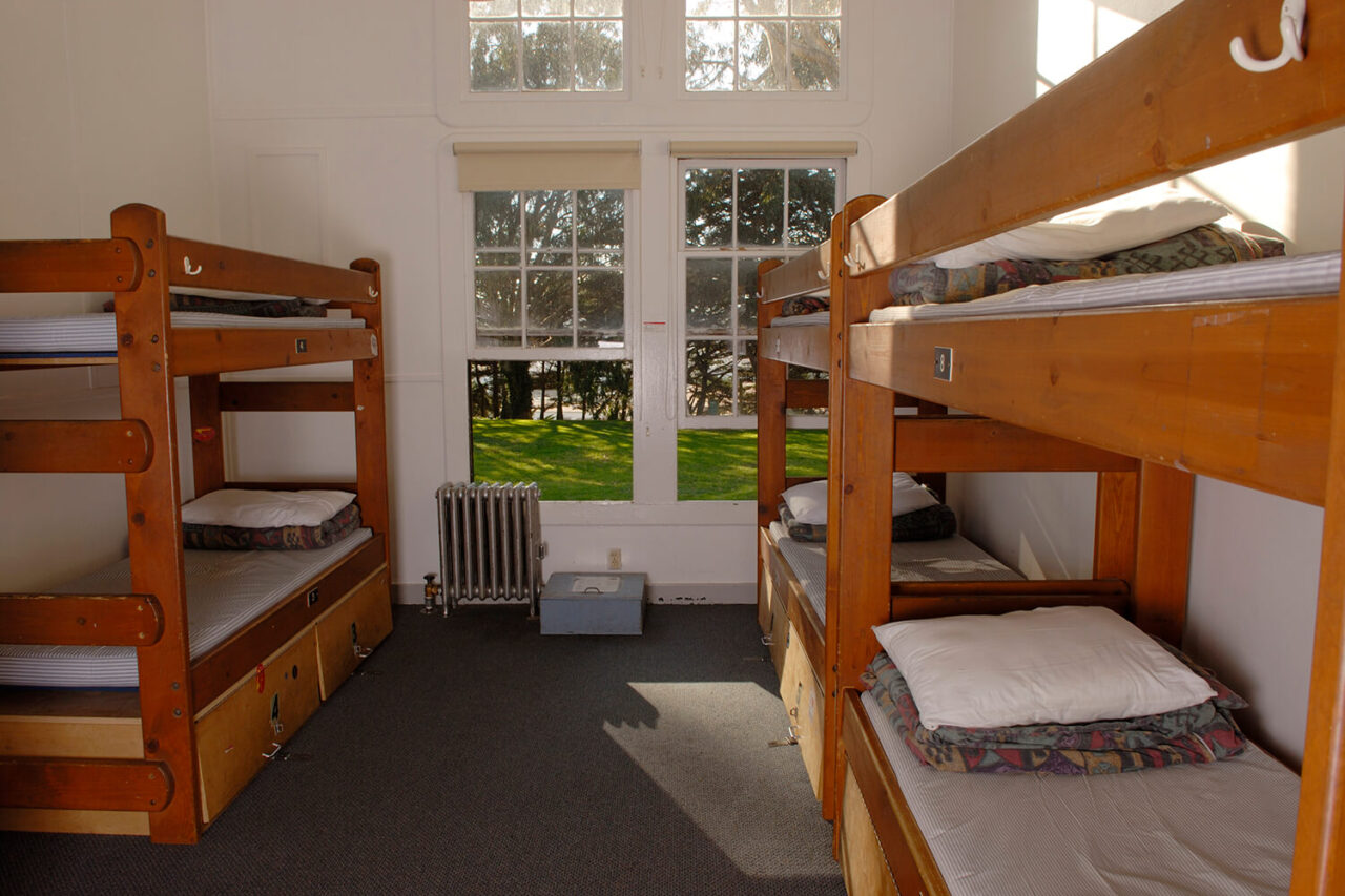 two sets of wooden bunk beds in a medium-sized dorm room with a window looking out over the trees at HI San Francisco Fisherman's Wharf hostel