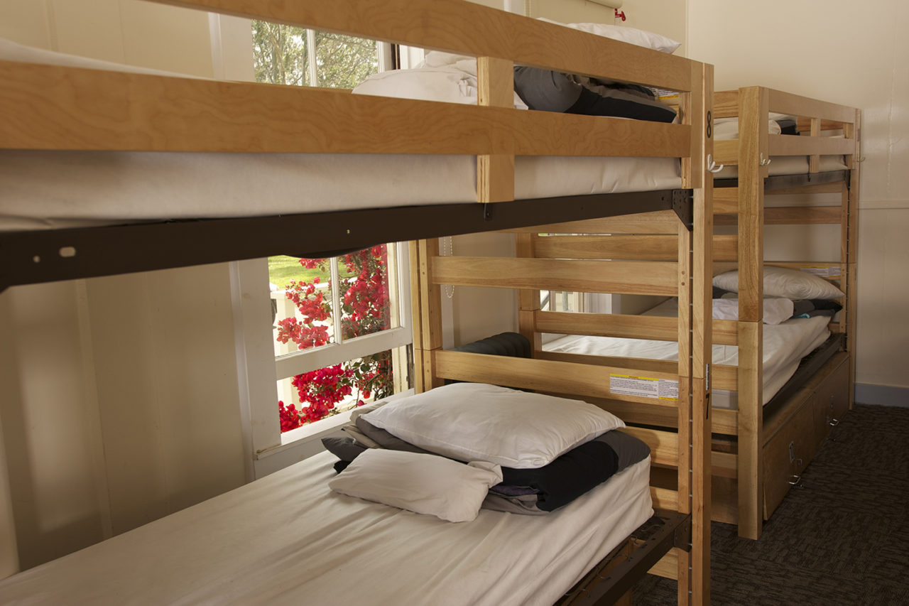 four wooden bunk beds with fresh linens in a dorm room with a view of pink flowers out the window at HI San Francisco Fisherman's Wharf hostel