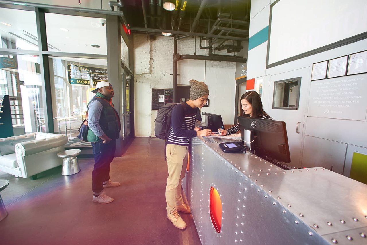 a friendly front desk agent checks in a guest at the front desk of HI Boston hostel