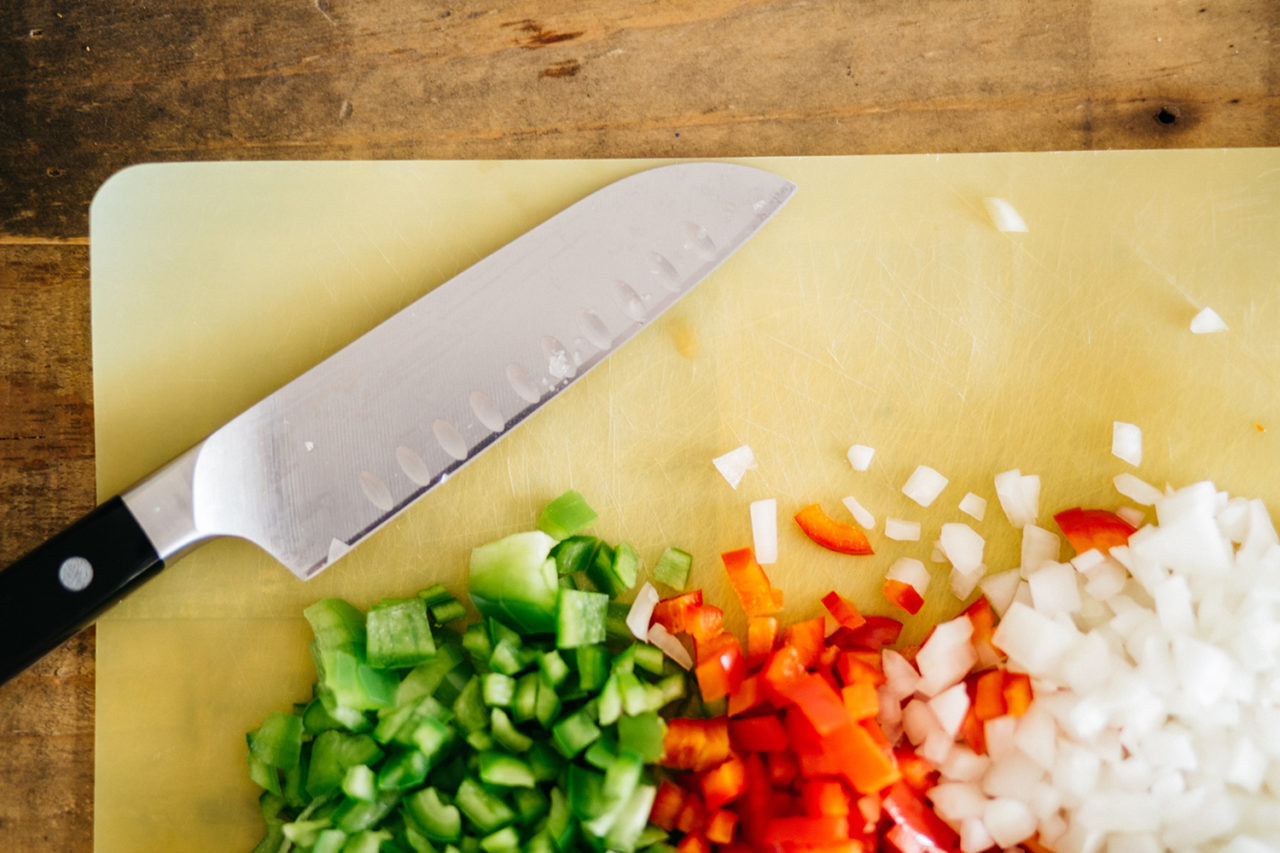 HI San Francisco Fisherman's Wharf hostel has a fully equipped guest kitchen with everything groups need to make their own meals. In this photo, we see a yellow cutting board, a large knife, and three piles of chopped up peppers and onions.