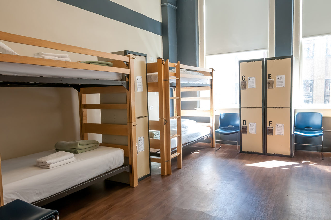 a dorm room at HI Chicago hostel with two sets of twin-sized bunkbeds, four individual secure lockers for guest belongings, and two large windows letting in plenty of natural light
