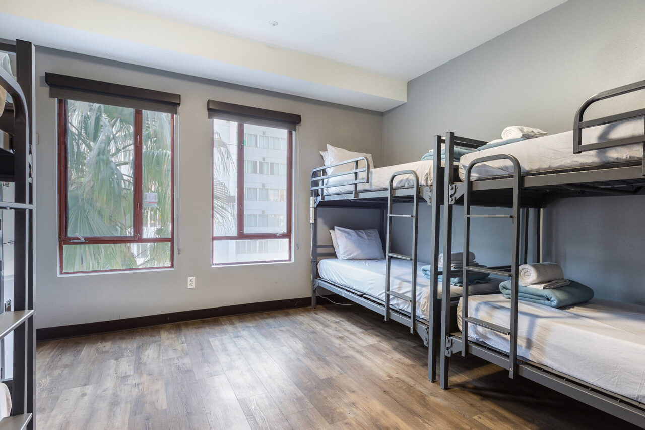 a spacious economy dorm at HI Los Angeles Santa Monica hostel. The sturdy bunkbeds have crisp white linens, there is hardwood flooring, and large windows look out over trees.