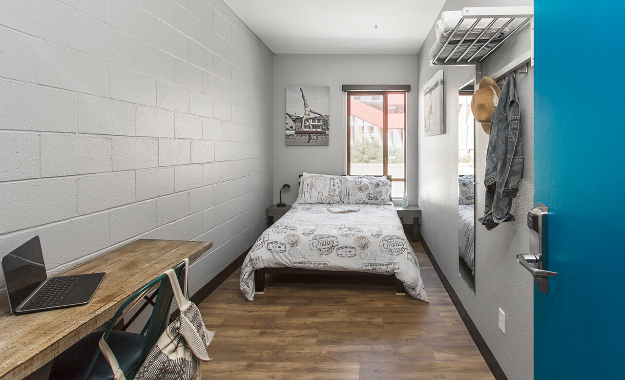 a freshly made full-sized bed in a small private room with a small desk and a chair inside HI Los Angeles Santa Monica hostel