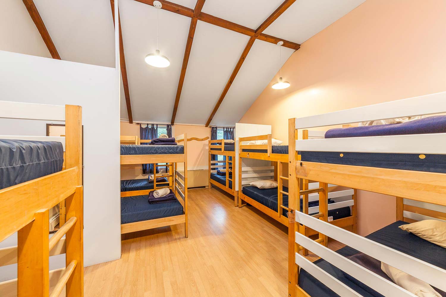 A large well lit dorm room at HI Martha's Vineyard hostel with five sets of twin-sized bunk beds, hardwood floors and high ceilings