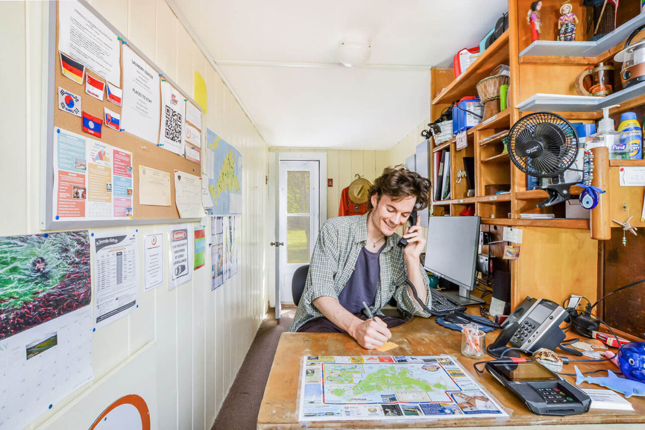 A friendly front desk agent at HI Martha's Vineyard hostel speaks on the phone while taking notes
