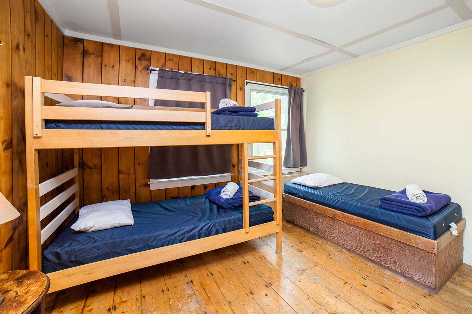 a bedroom at HI Martha's Vineyard hostel with hardwood floors and wood wall paneling, one set of twin-sized bunk beds, and one single twin-sized bed.