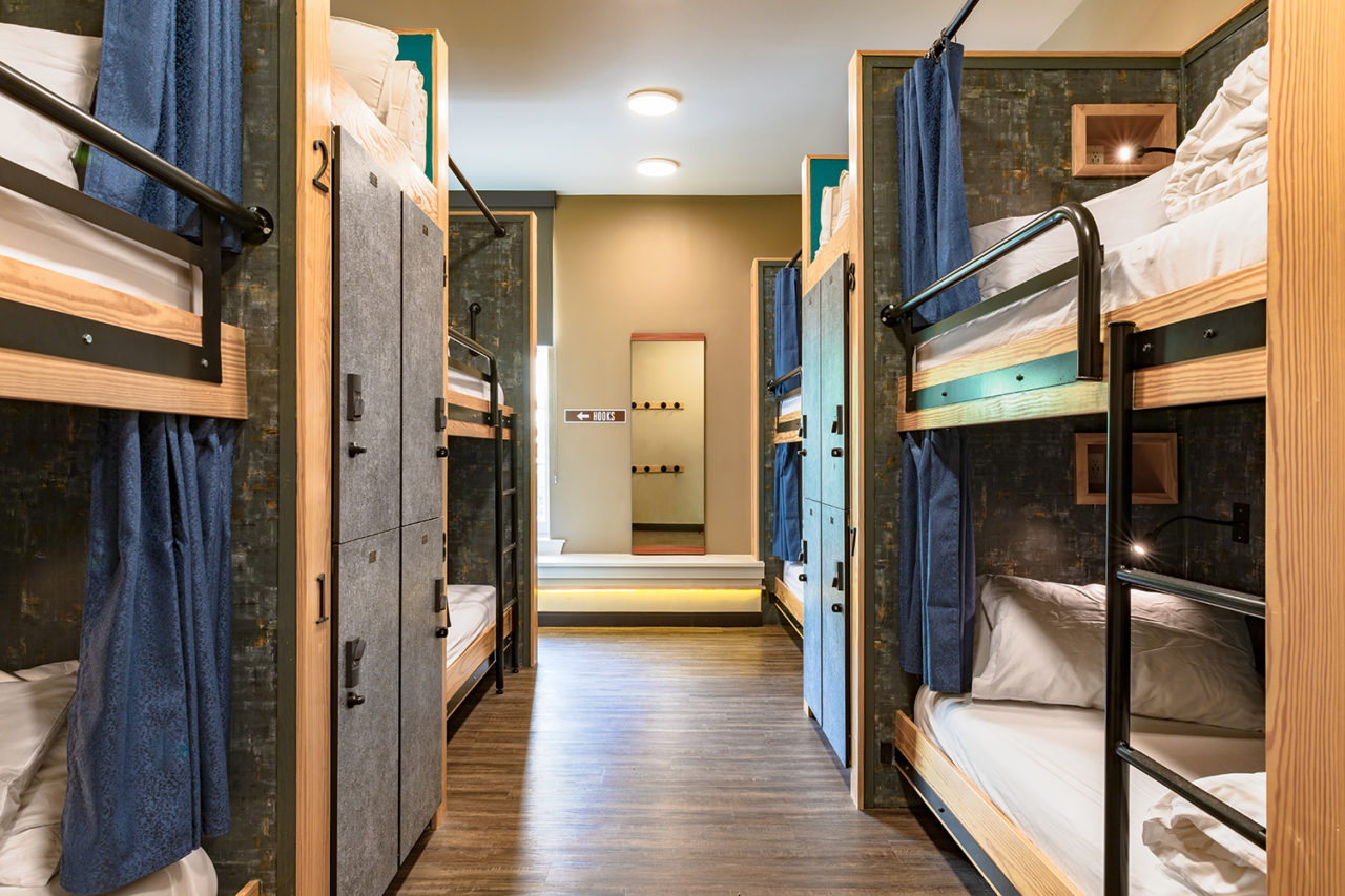 A dorm room at HI New Orleans hostel with four sets of twin-sized bunk beds. Each bed has a privacy curtain, and secure lockers for guests' belongings separate each set of bunks for added privacy. The beds are made up with crisp white linens and each has a built-in reading light at the head.