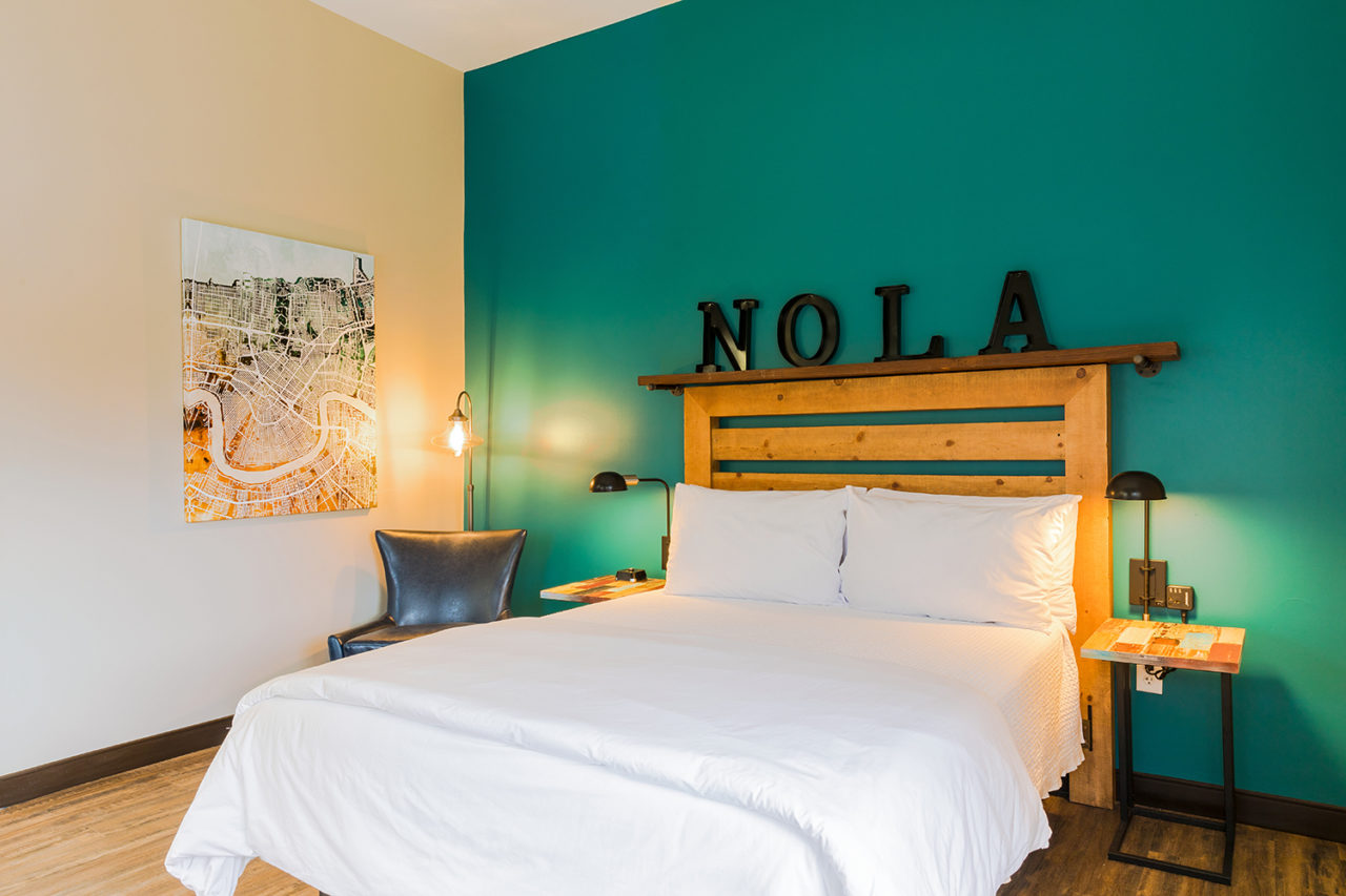 a queen-sized bed with clean linens and a bedside table with lamp and teal walls