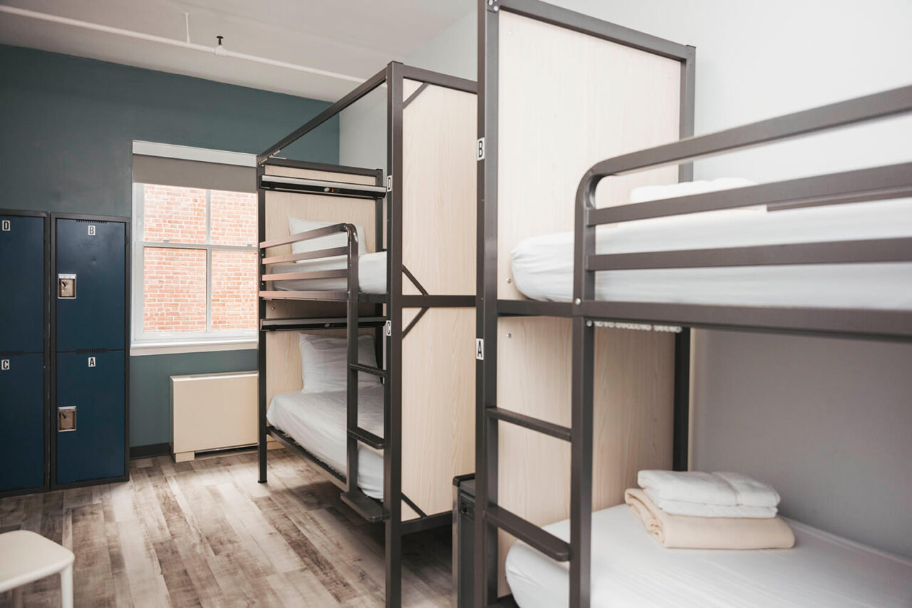 two sets of twin-sized bunk beds with privacy screens between them in a dorm room with hardwood floors and turquoise walls at HI New York City hostel