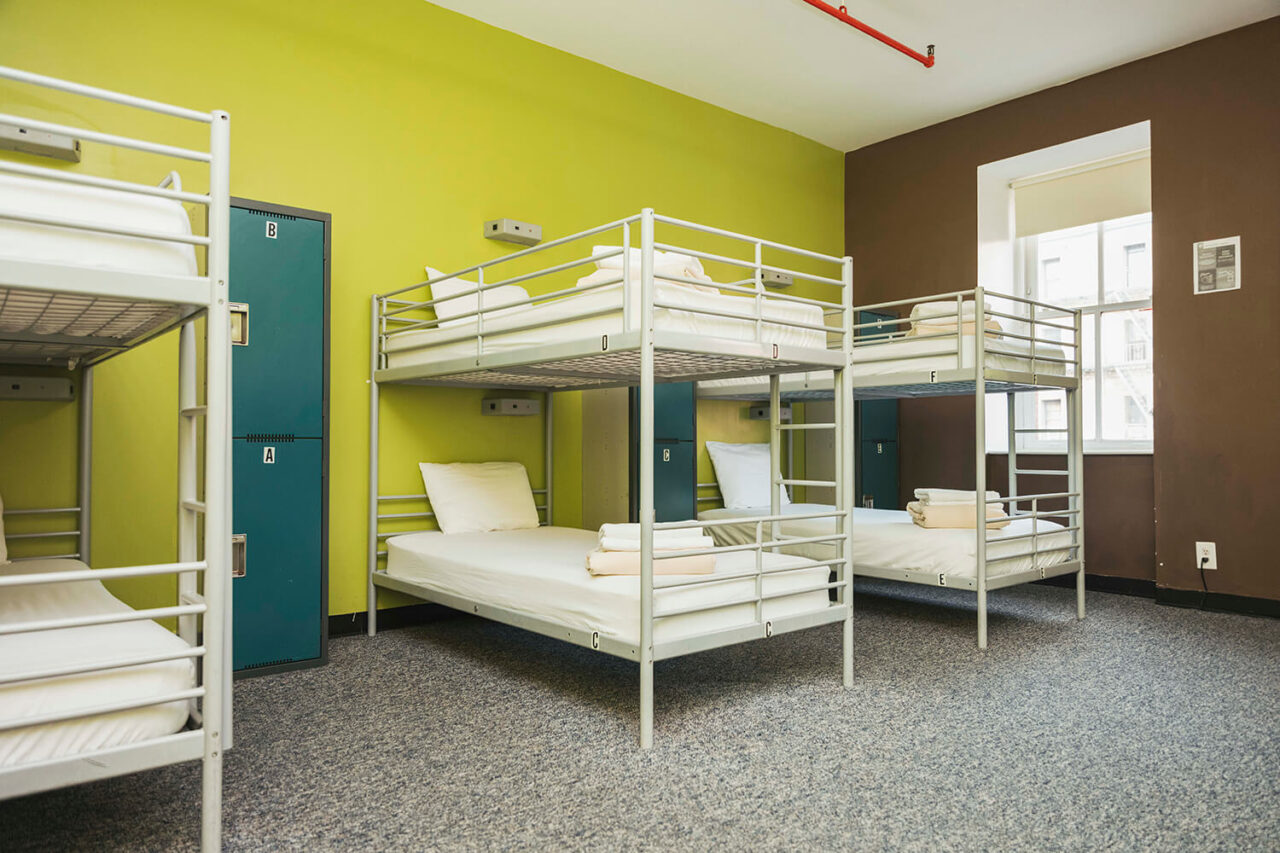 An economy dorm room at HI New York City hostel with three sets of bunk beds with crisp white linens, secure lockers for guest belongings, and green walls.