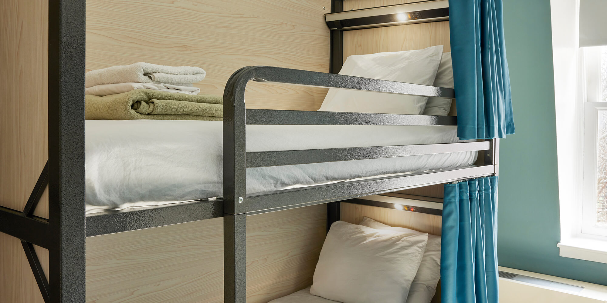 a set of twin-sized bunk beds with clean white linens, privacy screens, privacy curtains, and individual reading lights and charging ports at HI New York City hostel