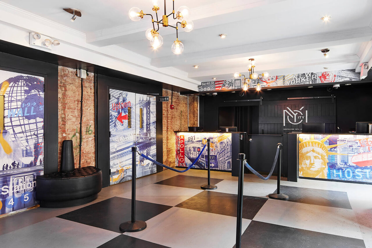 the lobby at HI New York City hostel features exposed brick walls, New York-themed murals, and black and white checkered flooring