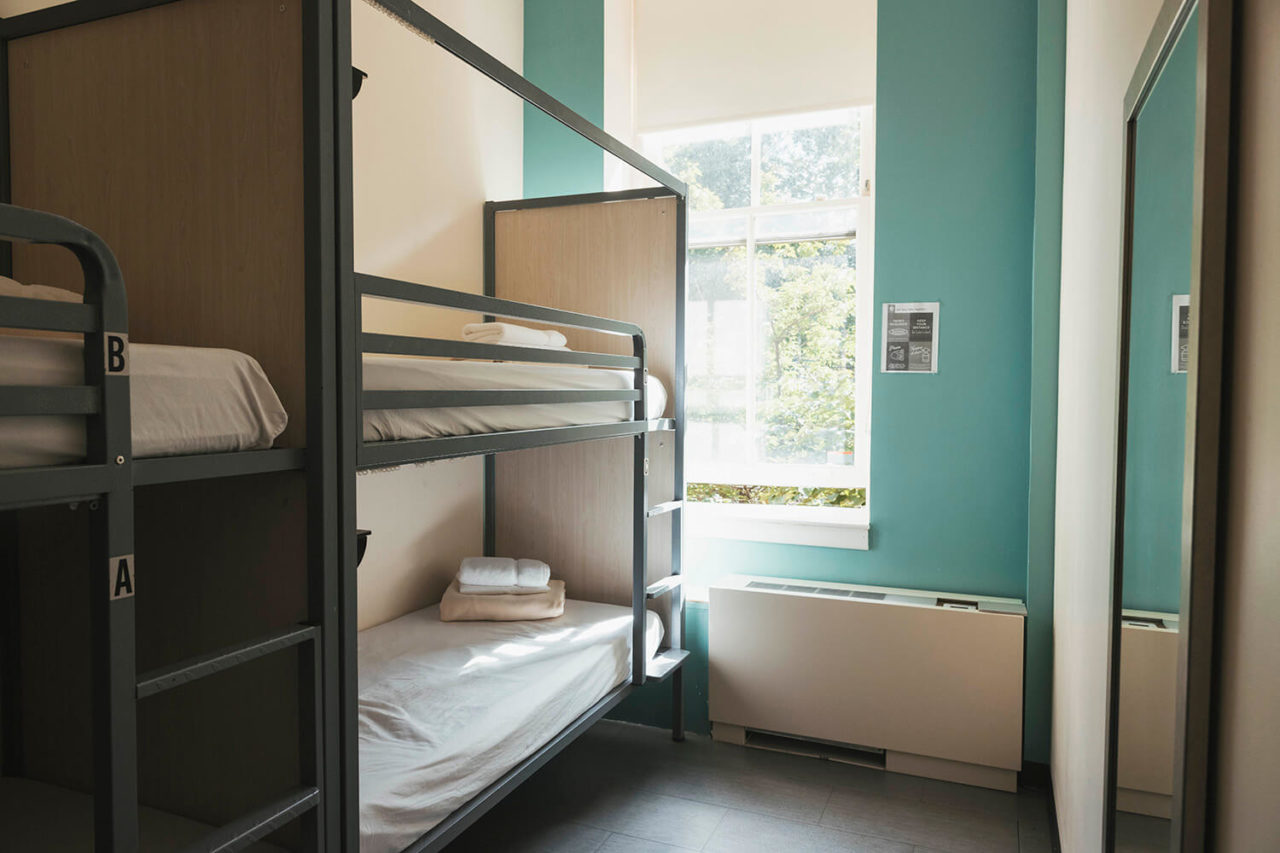 two sets of bunk beds with privacy barriers between them in a room with teal colored walls at HI New York City hostel