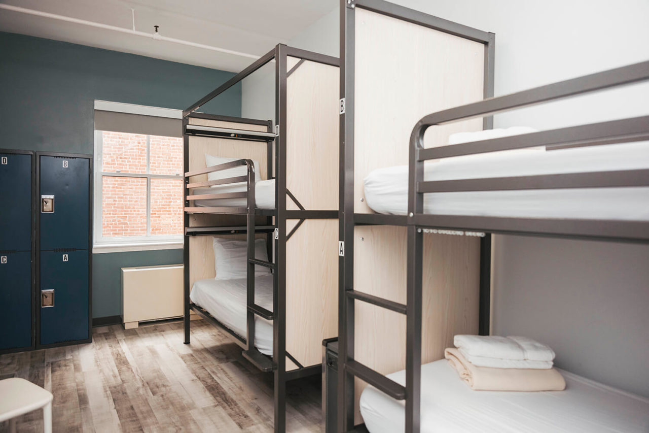 Two sets of freshly made bunk beds in a well lit room with wood floors