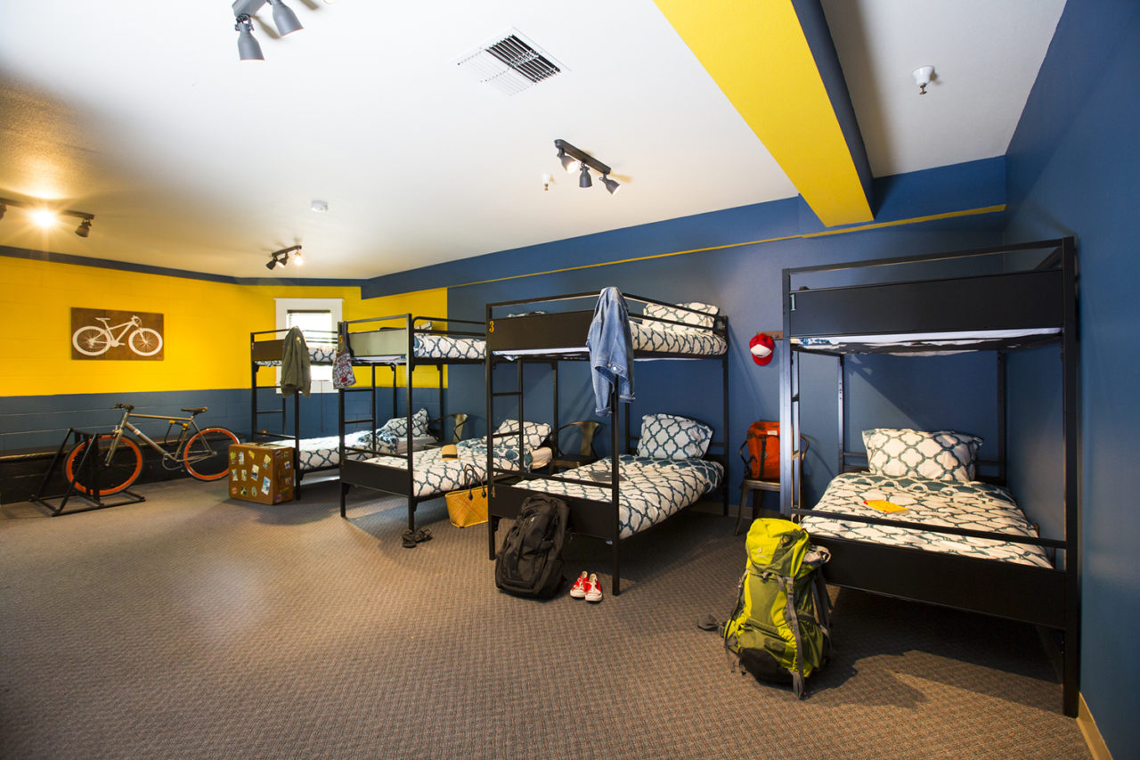 a dorm room at HI Sacramento hostel with four sets of twin-sized bunk beds. The walls are yellow and blue, and there are backpacks and other personal items hung up around the room.